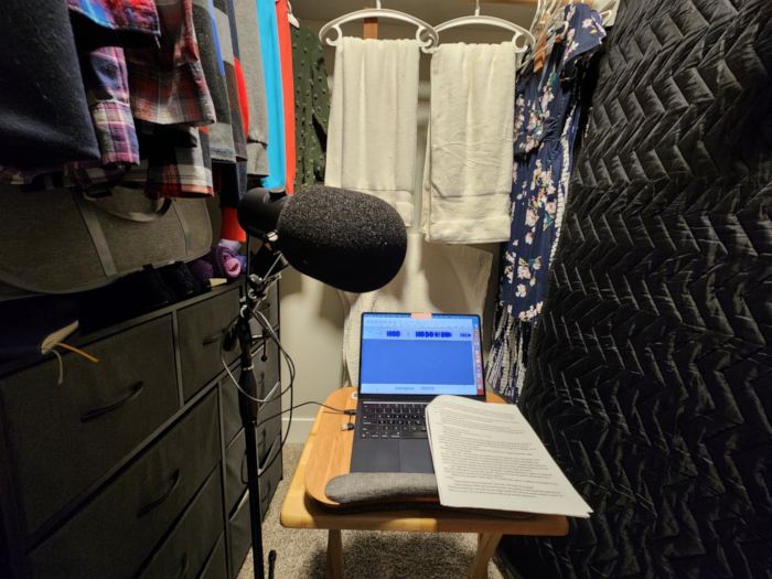 closet with clothes, blankets, and a table with a mic and laptop